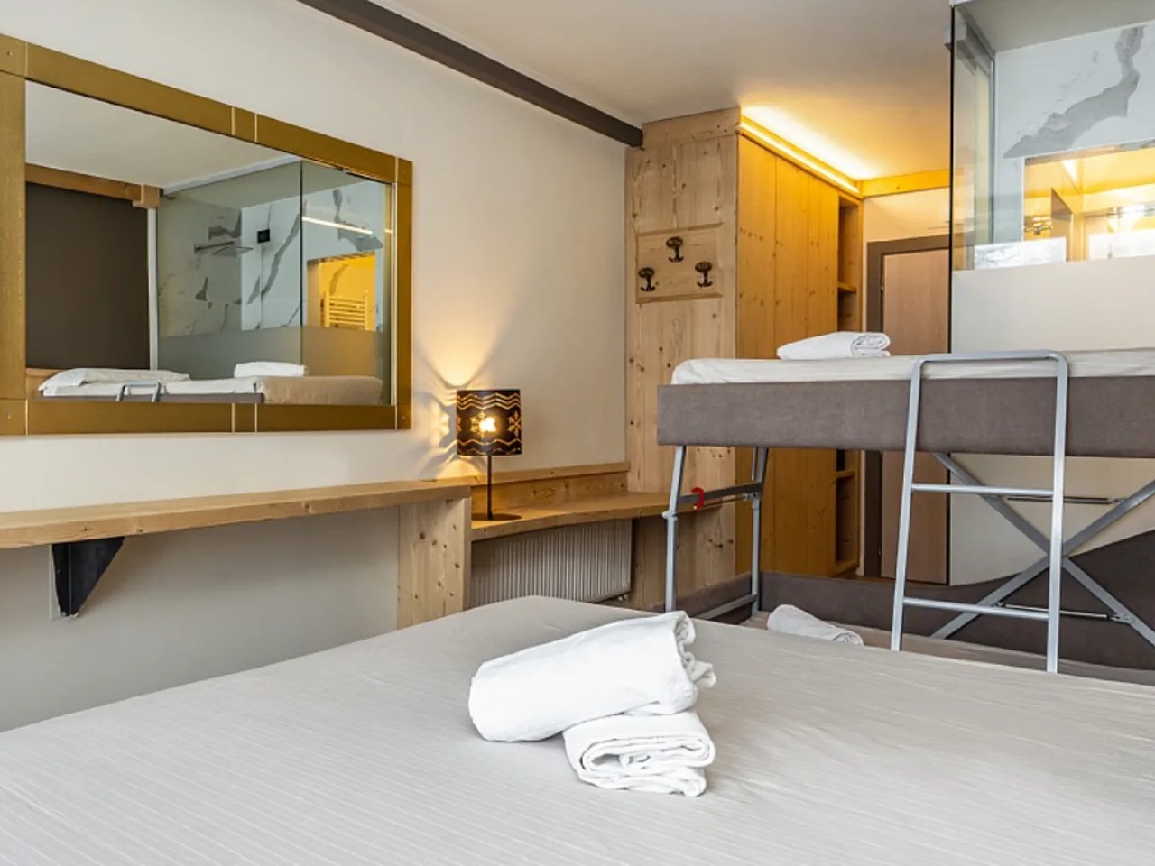 Nowoczesny pokój hotelowy w Hotelu Piandineve, Passo del Tonale, Włochy, z łóżkiem podwójnym i łóżkiem piętrowym, lustrem i drewnianym wykończeniem.