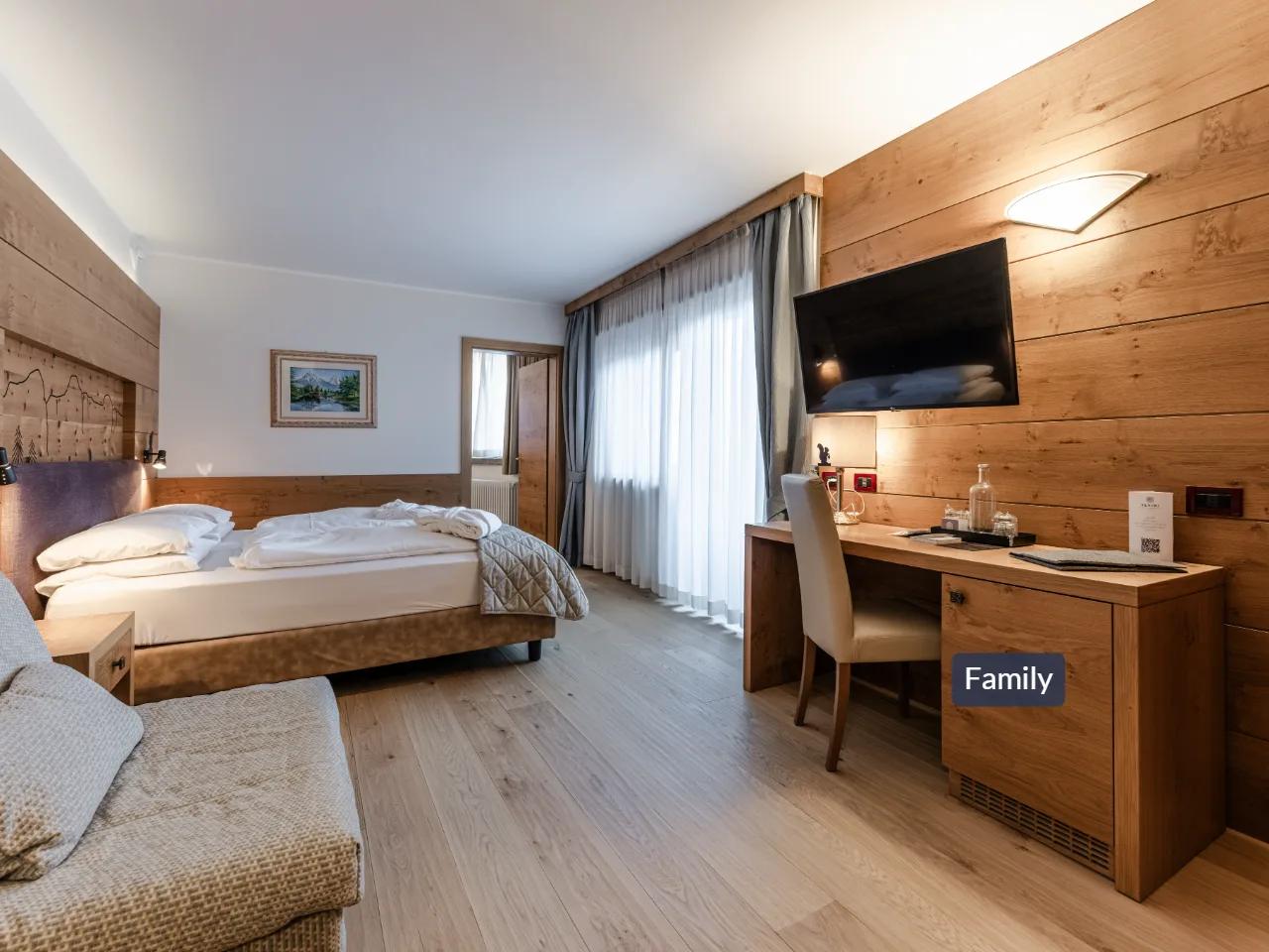 Jasny, nowoczesny pokój hotelowy z drewnianymi ścianami, wygodnym łóżkiem, biurkiem i telewizorem, idealny dla rodzin.