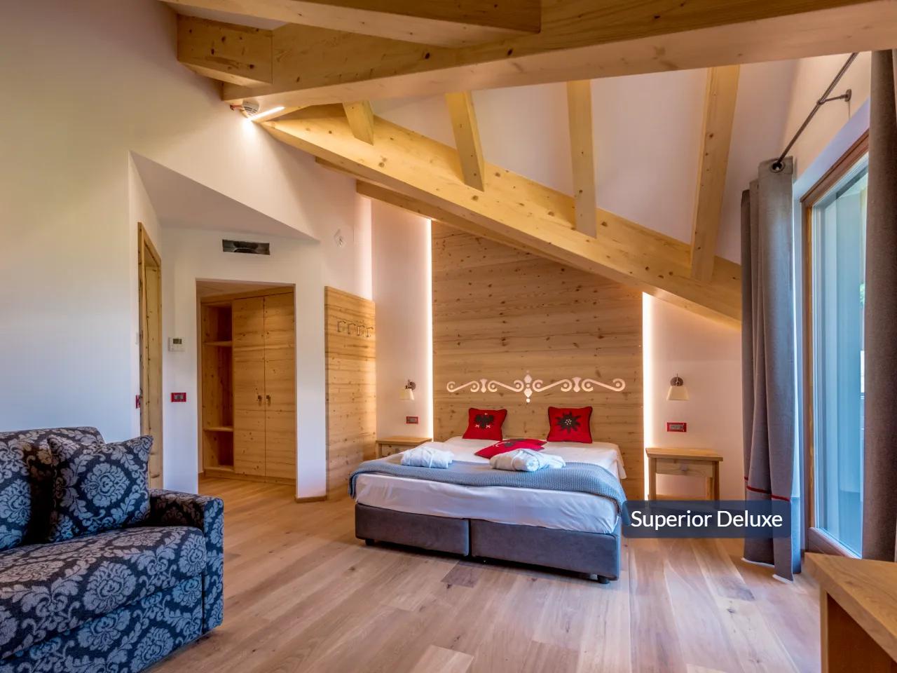 Komfortowy pokój Superior Deluxe w TEVINI, Val di Sole, Włochy. Eleganckie drewniane wnętrze, duże łóżko, sofa i okno.