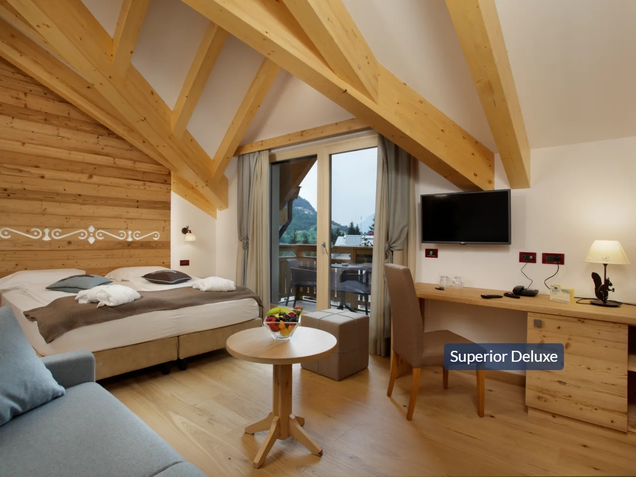 Przytulny pokój Superior Deluxe w hotelu Tevini z drewnianym sufitem, komfortowym łóżkiem i widokiem na góry Val di Sole.