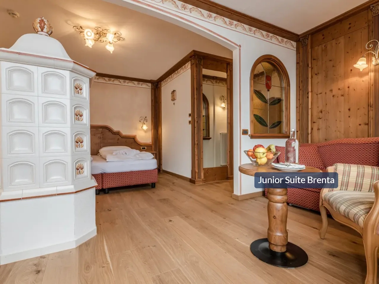 Przytulny pokój w Tevini, Val di Sole, Włochy. Widok na piec kaflowy, łóżko, drewniane ściany i kącik wypoczynkowy.