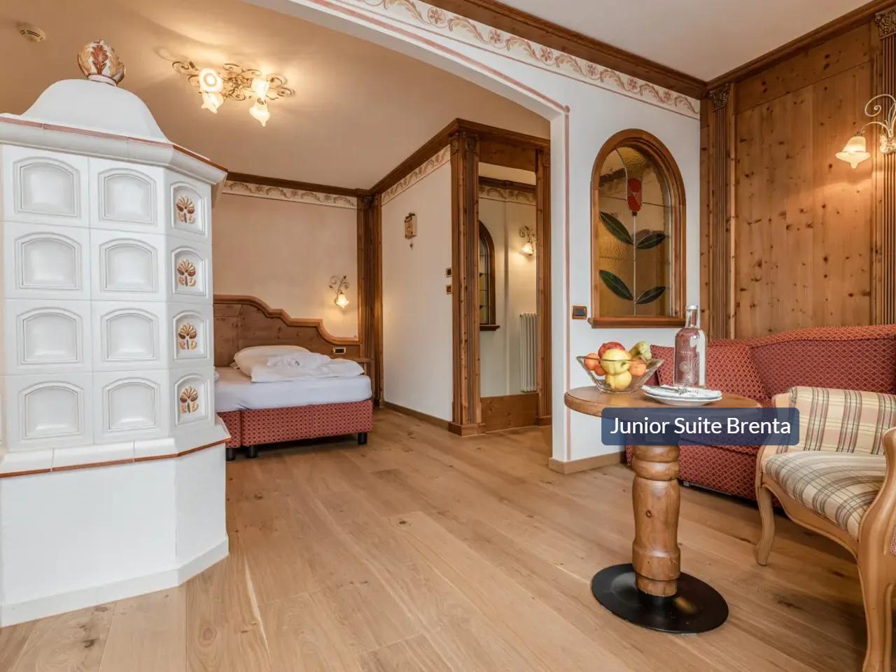 Przytulny pokój w Tevini, Val di Sole, Włochy. Widok na piec kaflowy, łóżko, drewniane ściany i kącik wypoczynkowy.