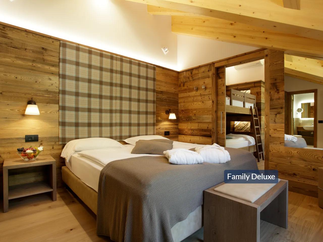 Luksusowy pokój rodzinny Family Deluxe w hotelu TEVINI Val di Sole, Włochy. Drewniane wnętrza, łóżko podwójne i łóżka piętrowe.