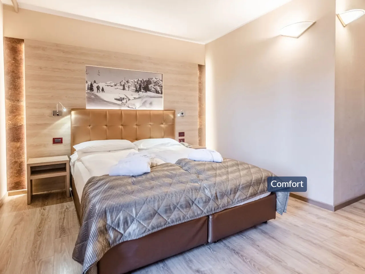 Komfortowy pokój hotelowy TEVINI Val di Sole, Włochy. Duże łóżko, drewniane panele, obraz górskiego krajobrazu, eleganckie wnętrze.