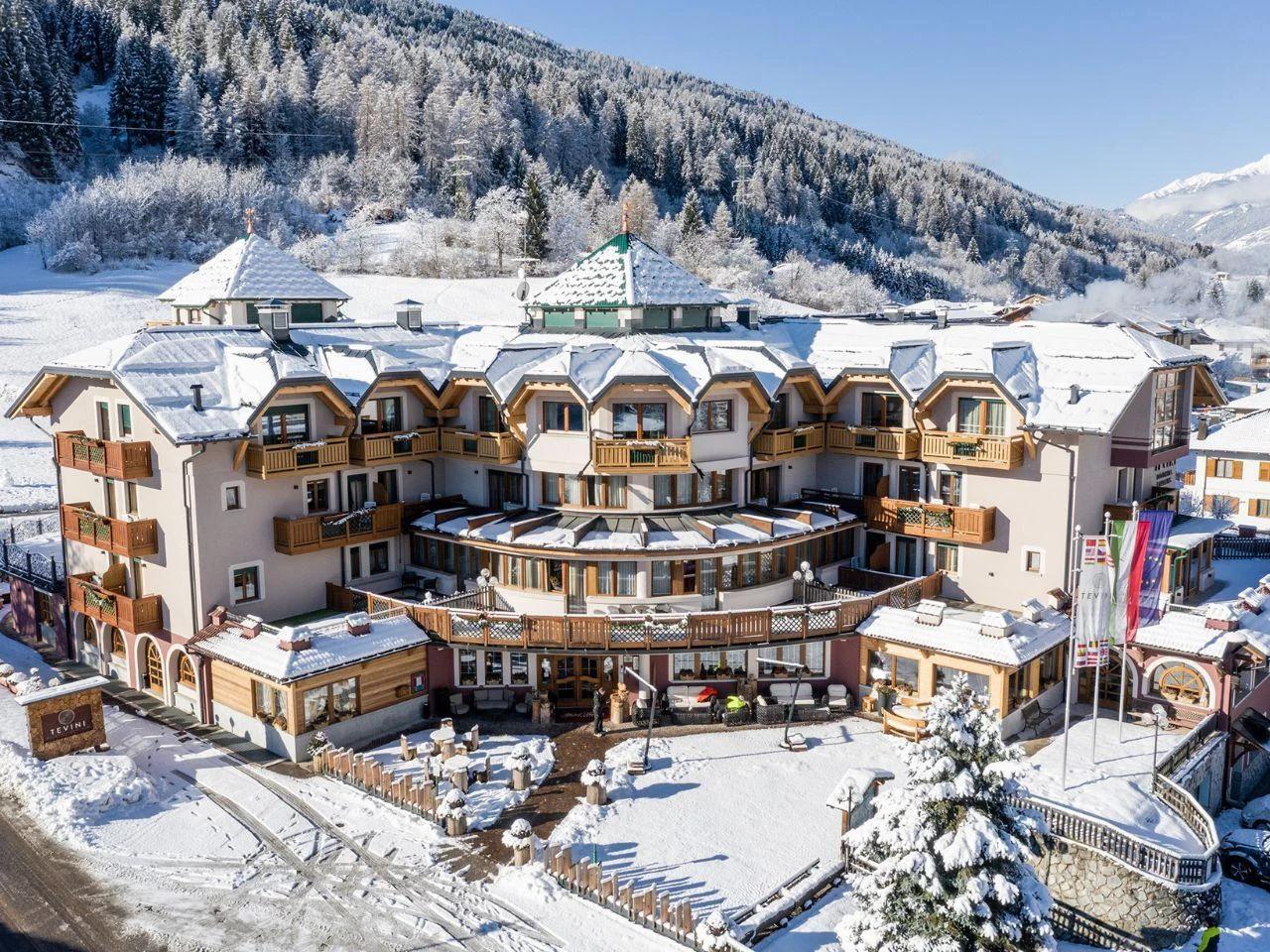Widok hotelu położonego w górskiej scenerii, z balkonami, tarasem oraz bezpośrednim otoczeniem ośnieżonych stoków i lasów.