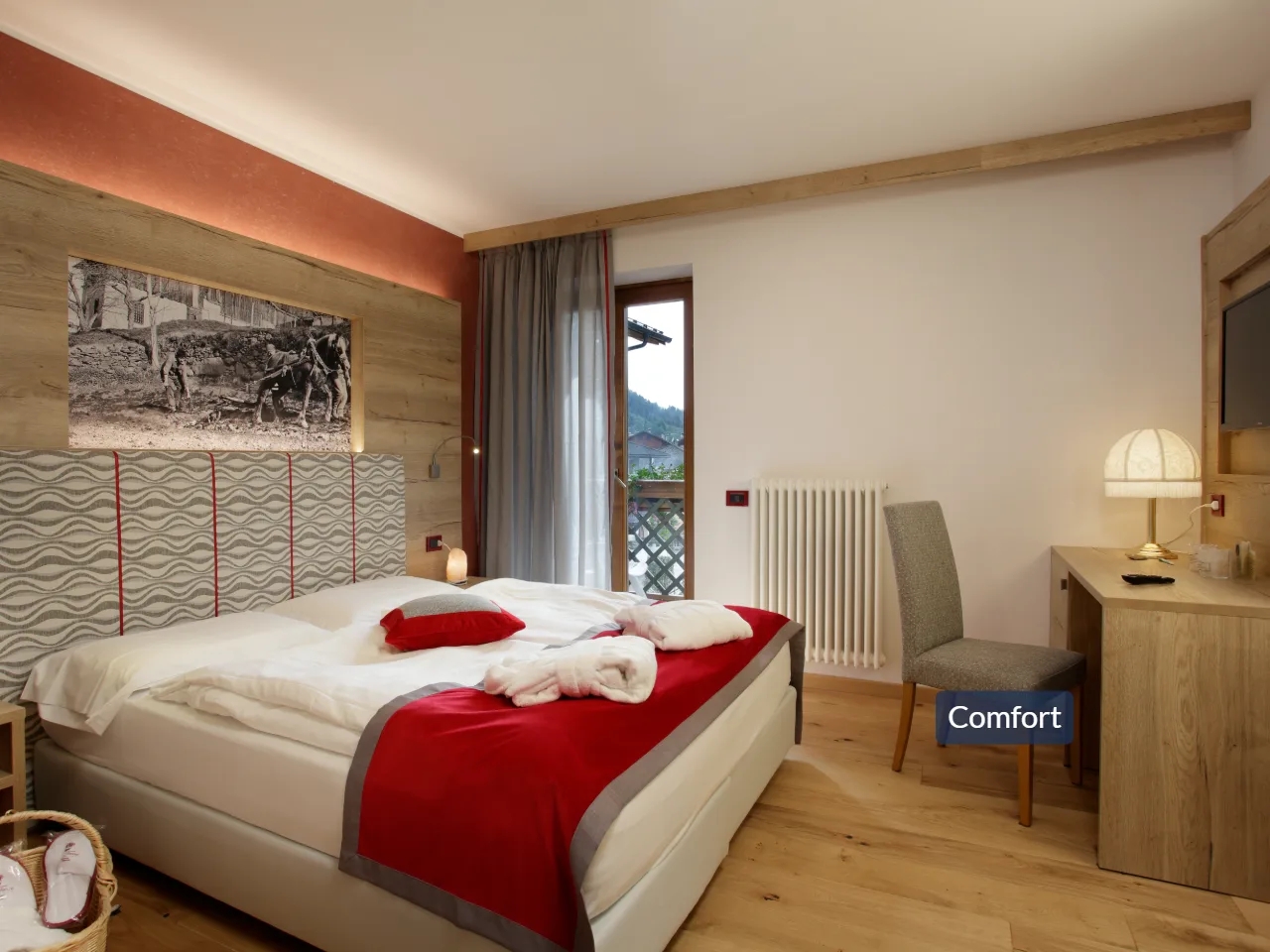 Komfortowy pokój w Hotelu TEVINI, Val di Sole, Włochy. Duże łóżko, drewniana podłoga, biurko i balkon.