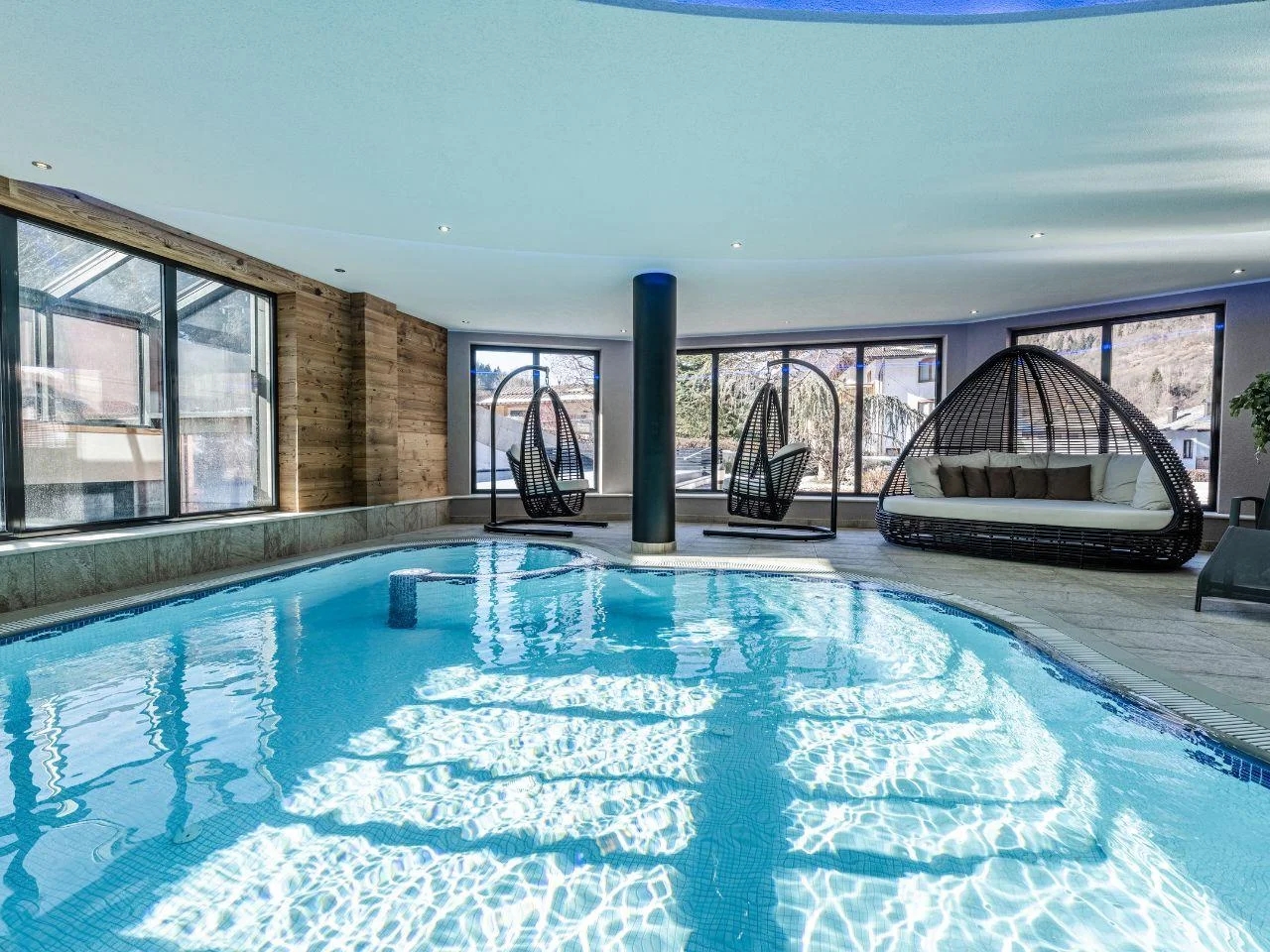 Strefa wellness z krytym basenem rekreacyjnym oraz leżankami wypoczynkowymi przy panoramicznych oknach.