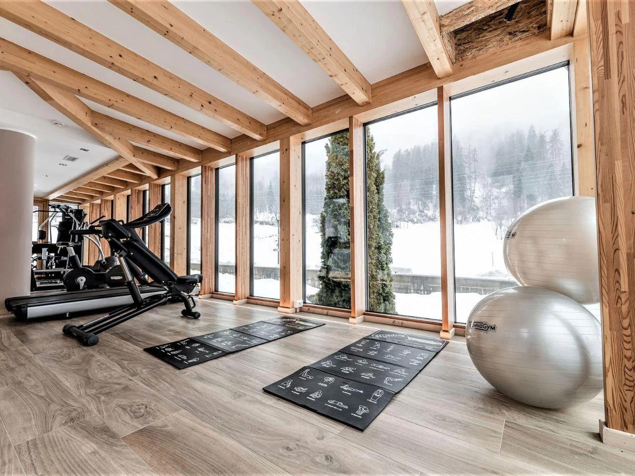 Nowoczesna siłownia w hotelu TEVINI, Val di Sole, Włochy. Panoramiczne okna, sprzęt TechnoGym, widok na ośnieżone góry.