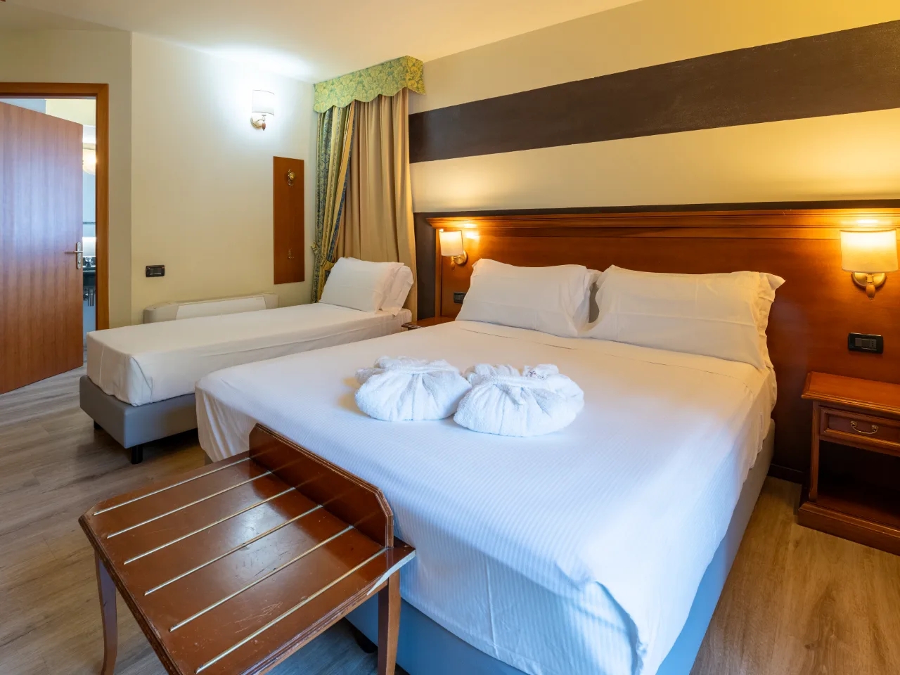 Przytulny pokój hotelowy w Hotelu Au Soleil w Aoście, Włochy. Podwójne łóżko, łóżko pojedyncze i eleganckie meble drewniane.