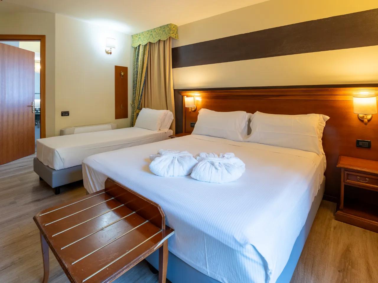 Przytulny pokój hotelowy w Hotelu Au Soleil w Aoście, Włochy. Podwójne łóżko, łóżko pojedyncze i eleganckie meble drewniane.