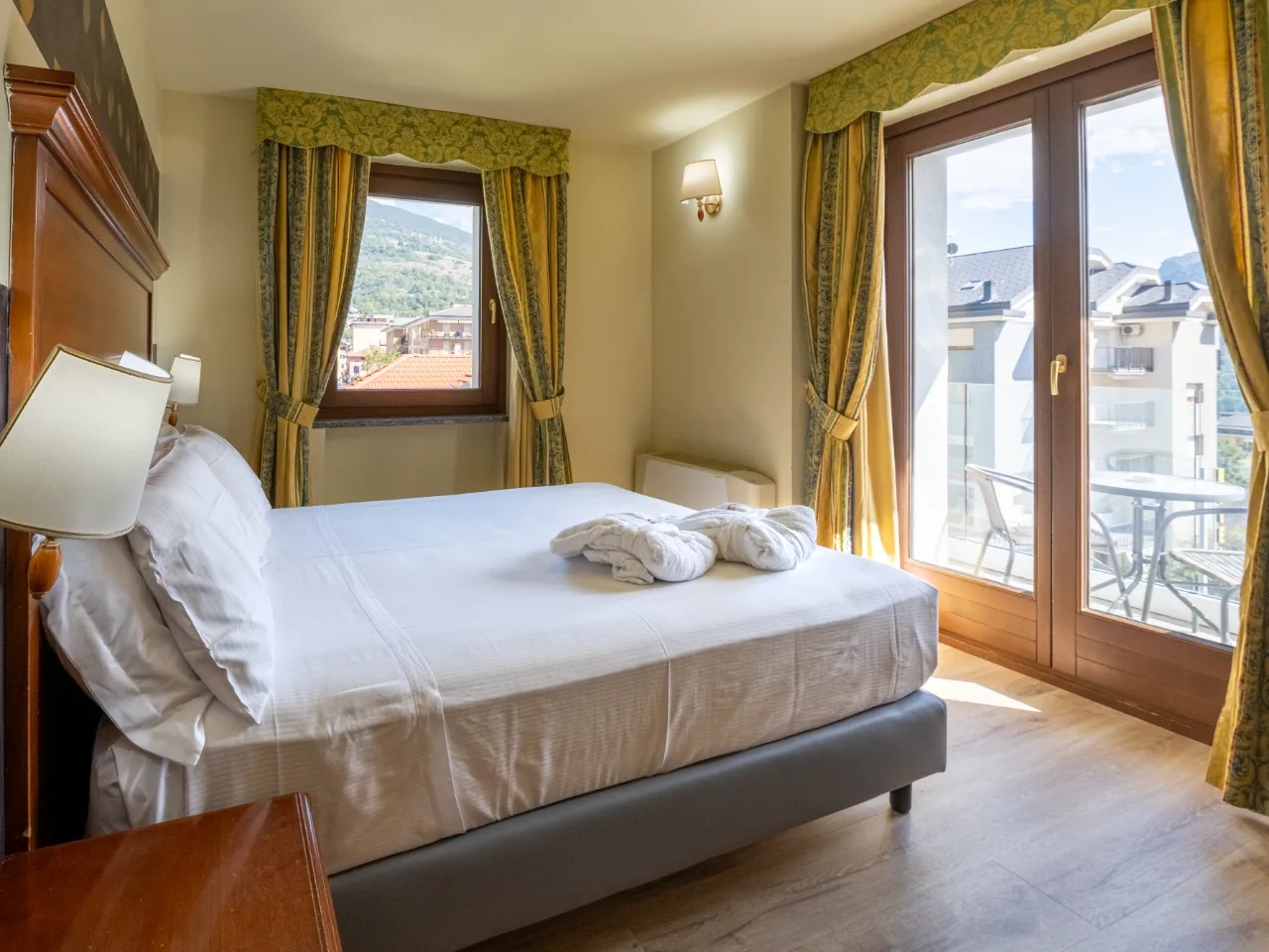 Przytulny pokój hotelowy w Hotelu Au Soleil Aosta z dużym łóżkiem, szlafrokami, widokiem na góry i balkonem.