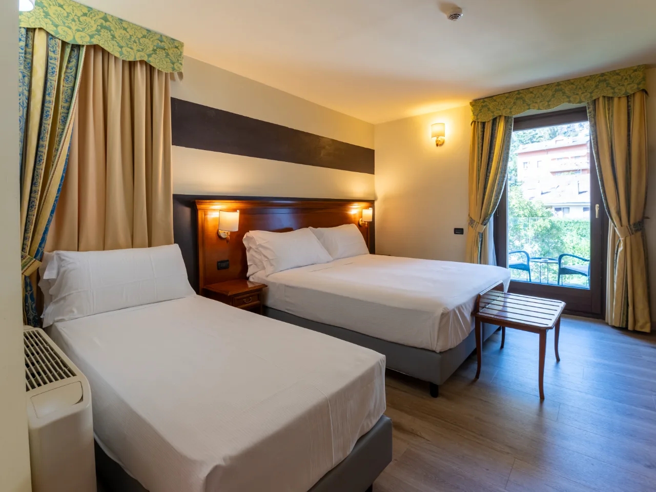 Pokój hotelowy w Hotelu Au Soleil w Aosta, Włochy z dużym łóżkiem podwójnym, łóżkiem pojedynczym, balkonem i jasnymi zasłonami.