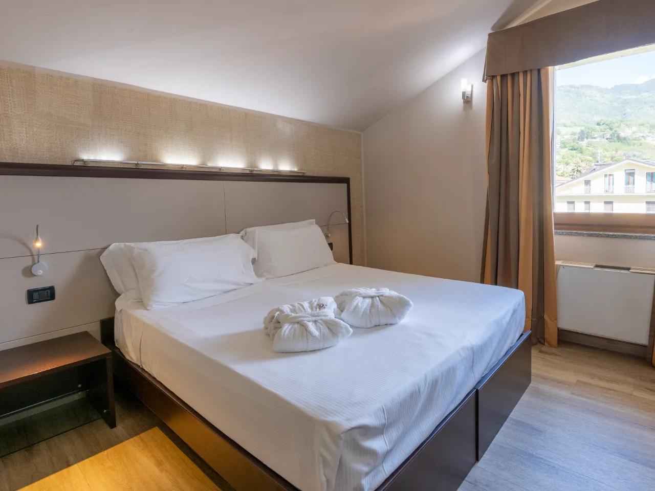 Komfortowy pokój w Hotel Au Soleil w Aosta, Włochy. Jasna sypialnia z dużym łóżkiem, szlafrokami i widokiem na góry.