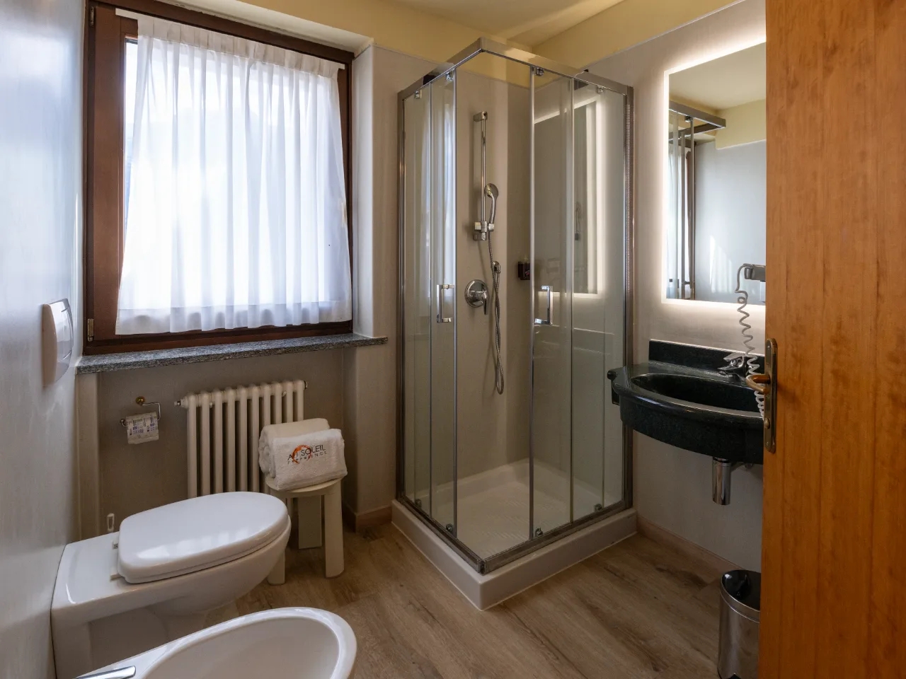 Jasna łazienka w Hotelu Au Soleil w Aoście z kabiną prysznicową, toaletą, bidetem i umywalką z lustrem LED.