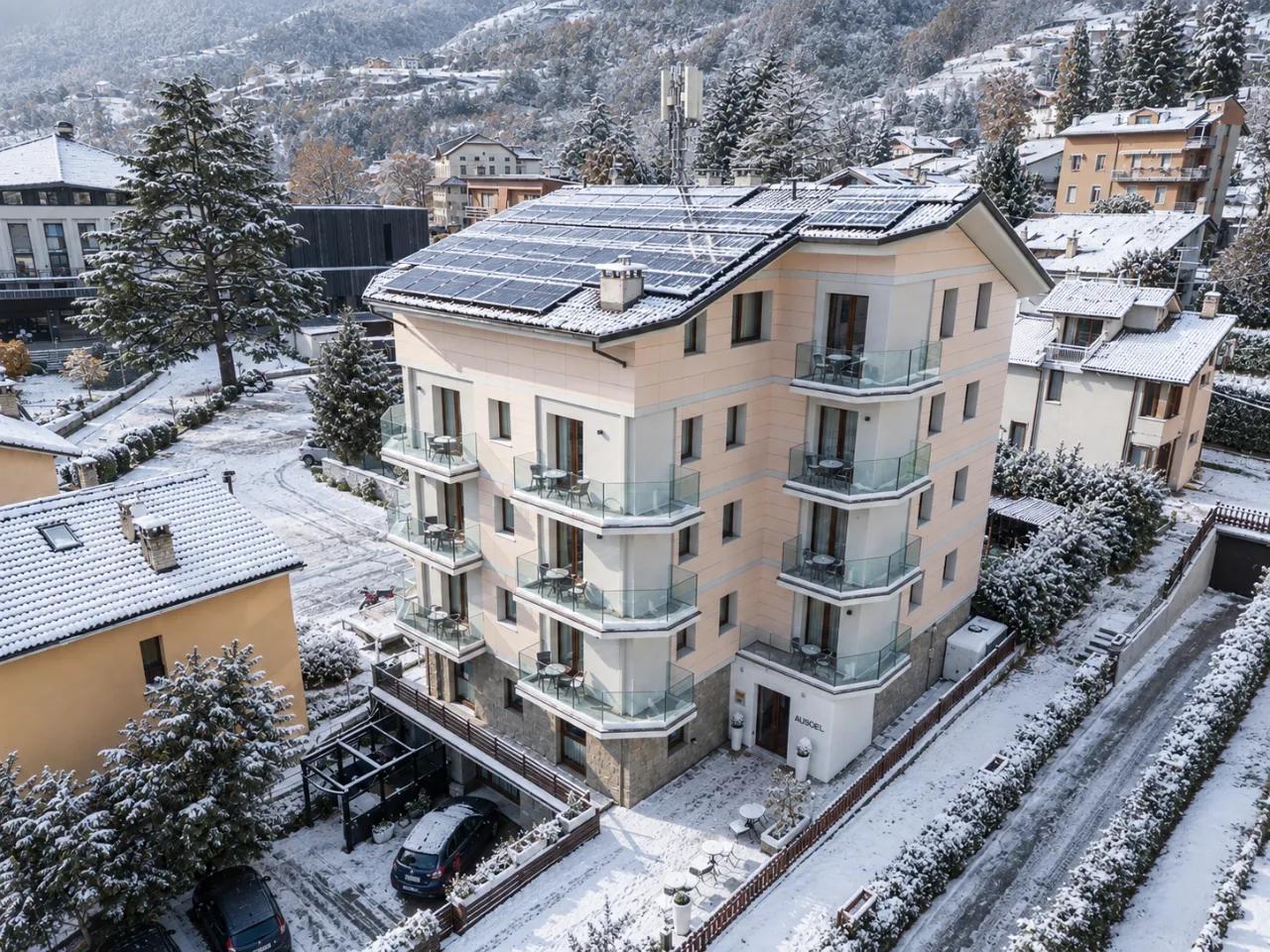Hotel Au Soleil w Aosta, Włochy, zimą. Budynek pokryty śniegiem, z panelami słonecznymi na dachu.