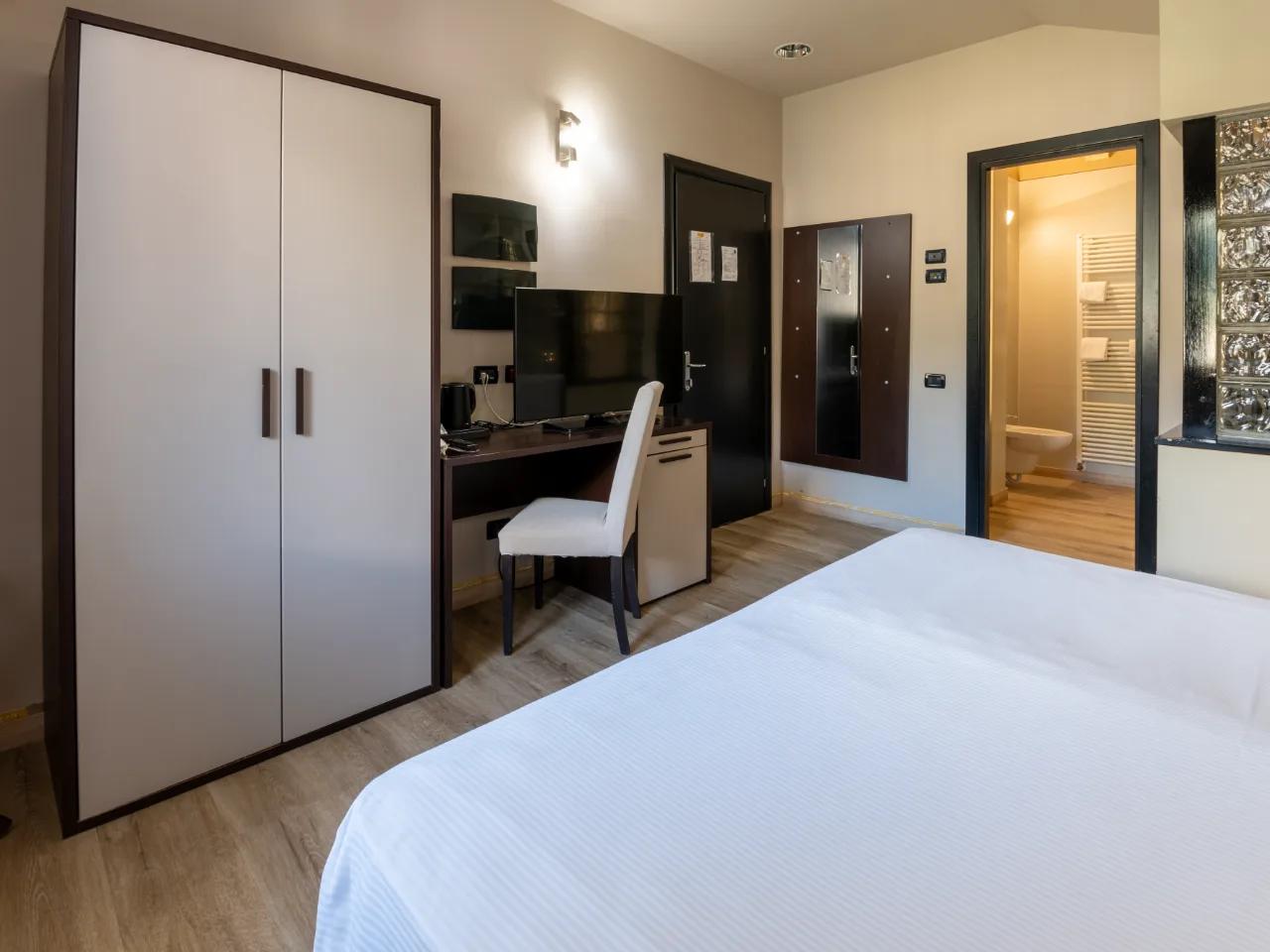 Pokój hotelowy w Hotelu Au Soleil Aosta, Włochy, z wygodnym łóżkiem, biurkiem z telewizorem i szafą, jasne wnętrze.