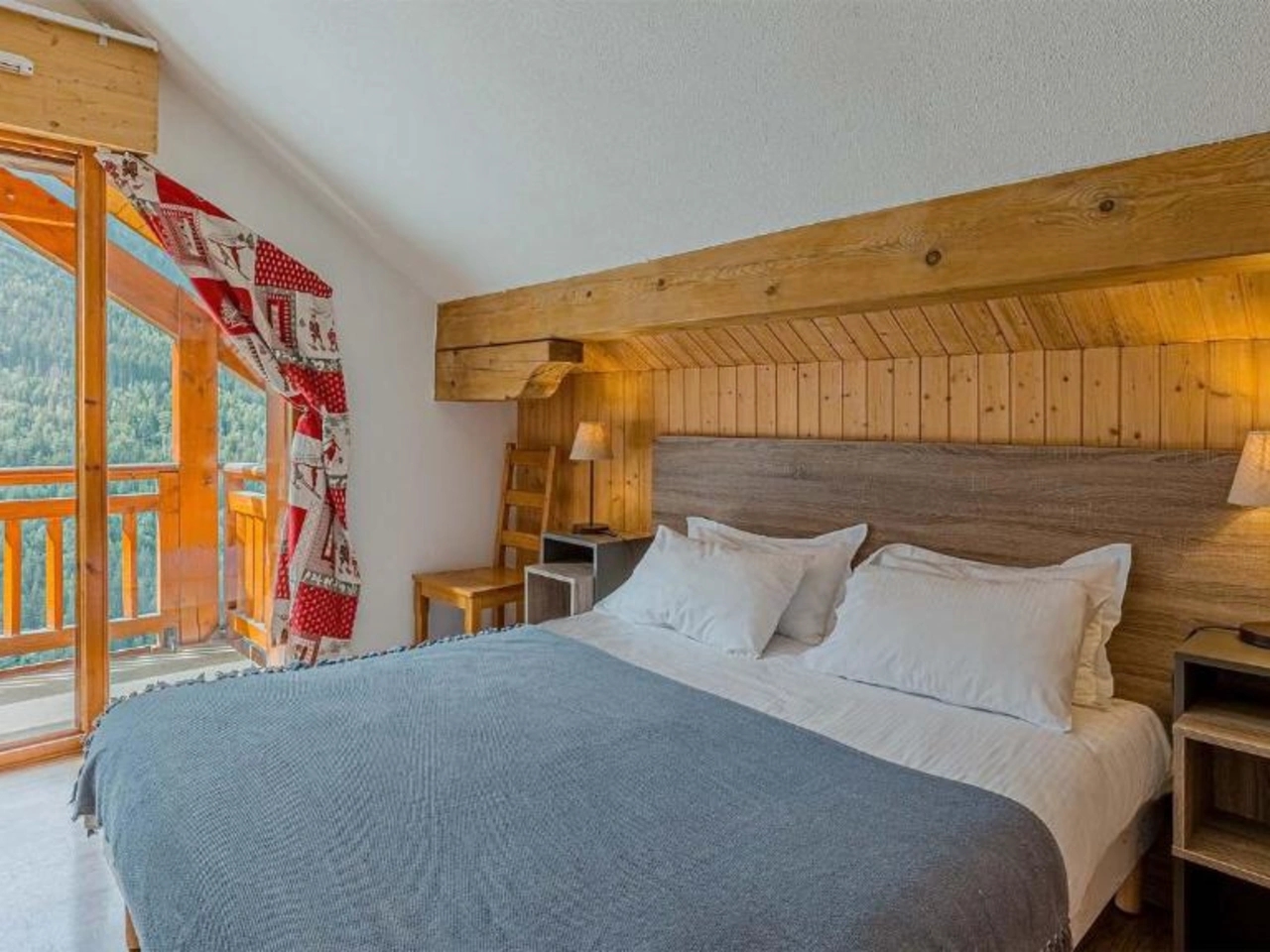 Sypialnia w La Cascade, Alpe D'Huez z łóżkiem małżeńskim, drewnianym wystrojem i balkonem z widokiem na Alpy.