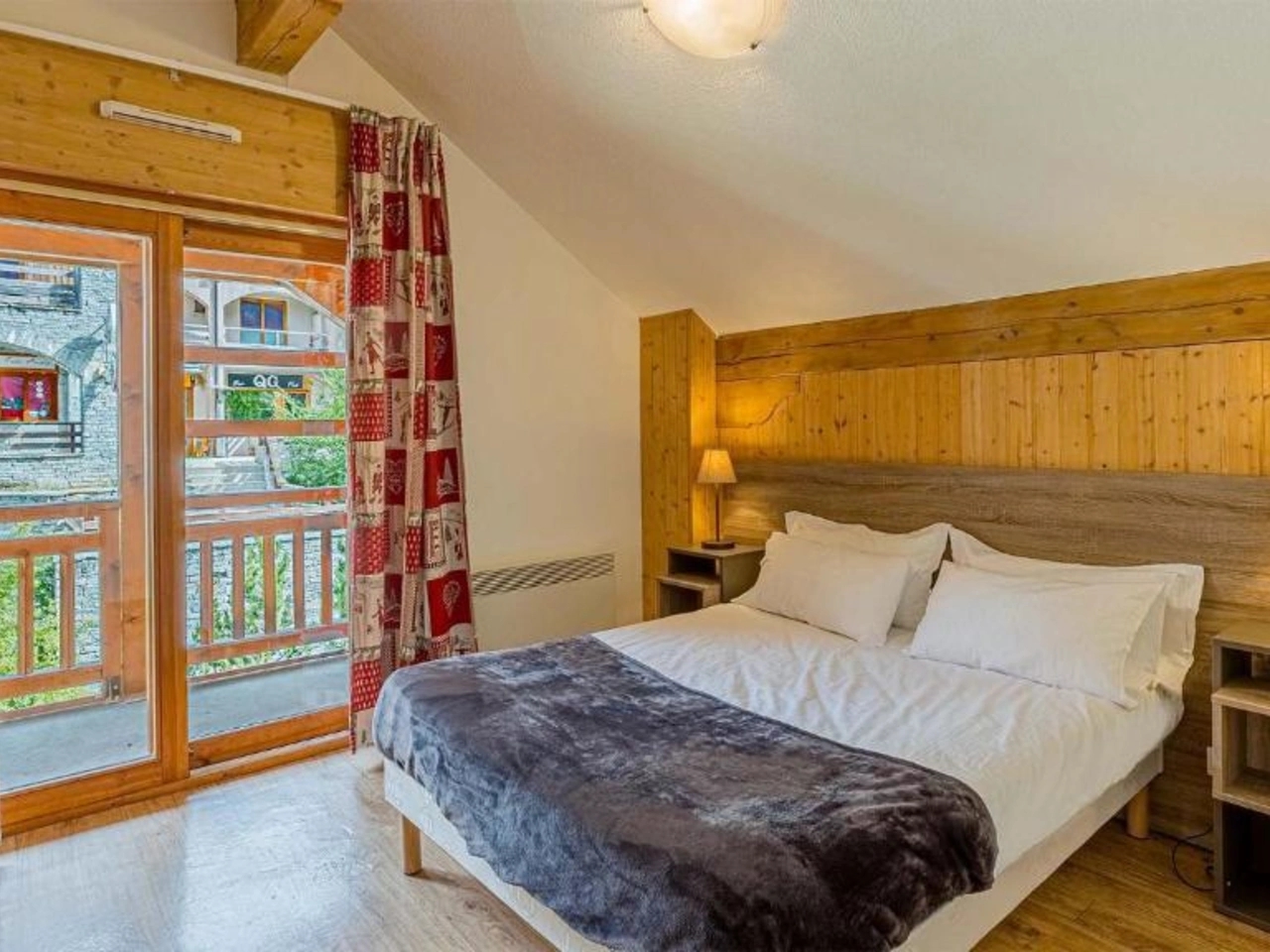 Przytulna sypialnia z łóżkiem, drewnianymi panelami, lampkami nocnymi i balkonem w La Cascade, Alpe D Huez, Francuskie Alpy.