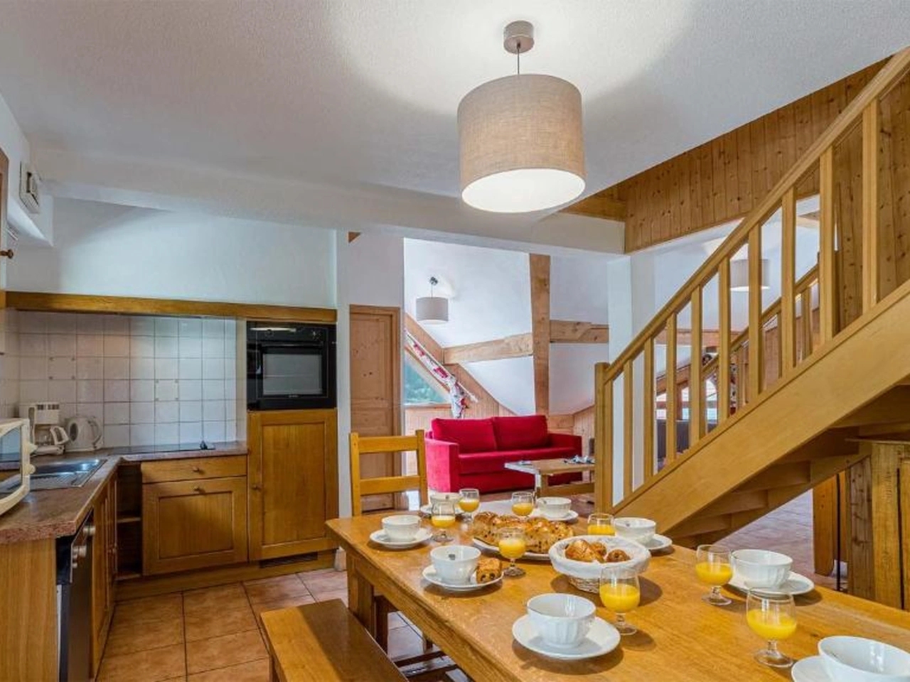 Przytulna jadalnia ze stołem śniadaniowym, aneksem kuchennym i salonem z czerwoną sofą w drewnianym apartamencie La Cascade w Alpe D'Huez.