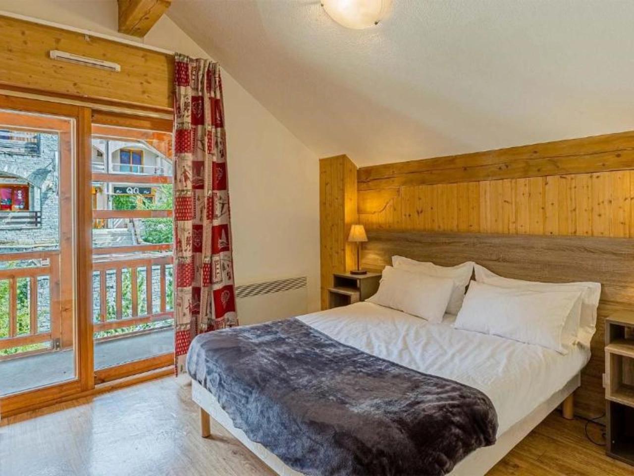 Przytulna sypialnia z łóżkiem, drewnianymi panelami, lampkami nocnymi i balkonem w La Cascade, Alpe D Huez, Francuskie Alpy.