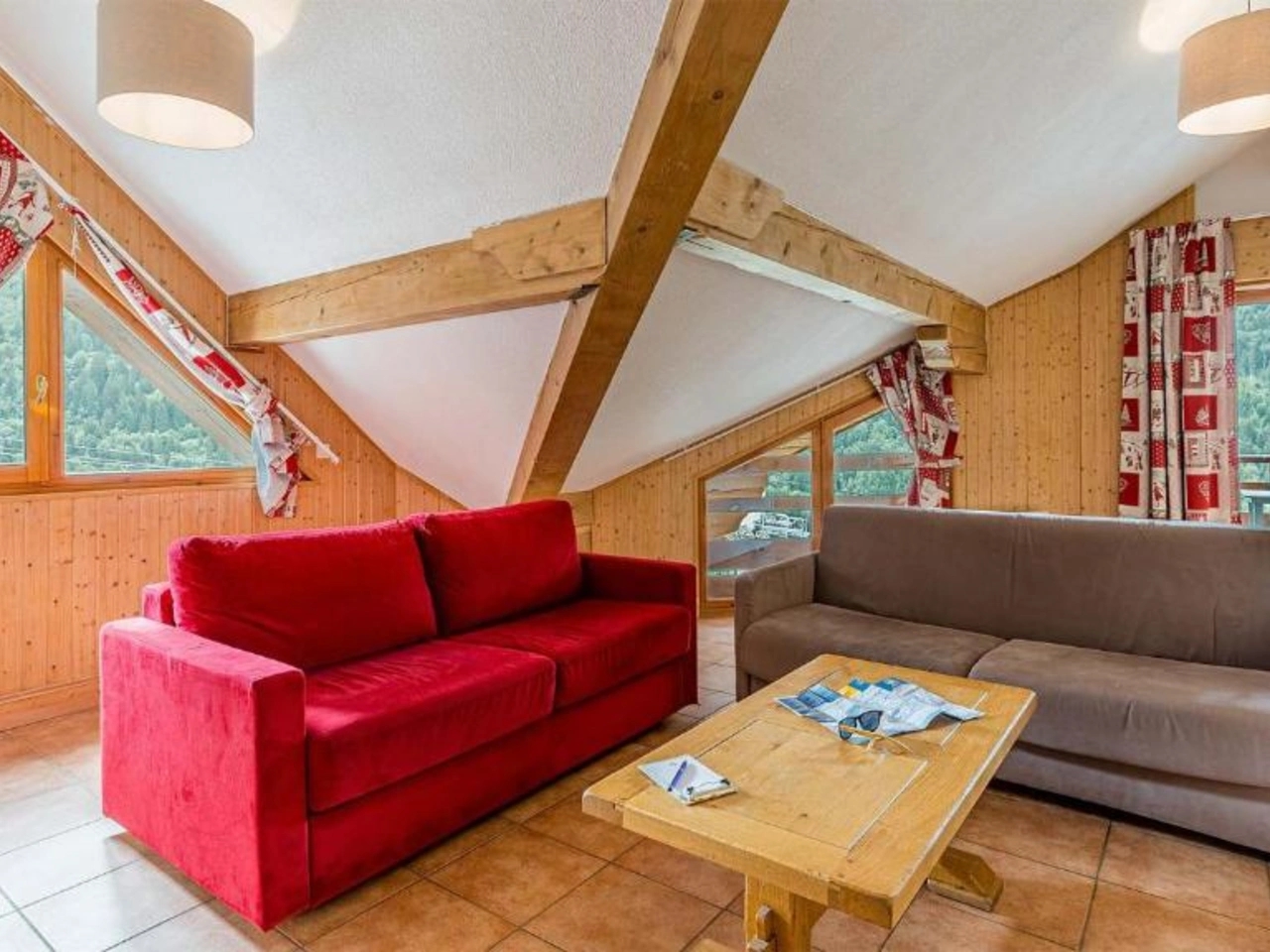 Przytulny salon w apartamencie La Cascade w Alpe D'Huez, z wygodnymi sofami, drewnianymi wykończeniami i malowniczym widokiem na góry.