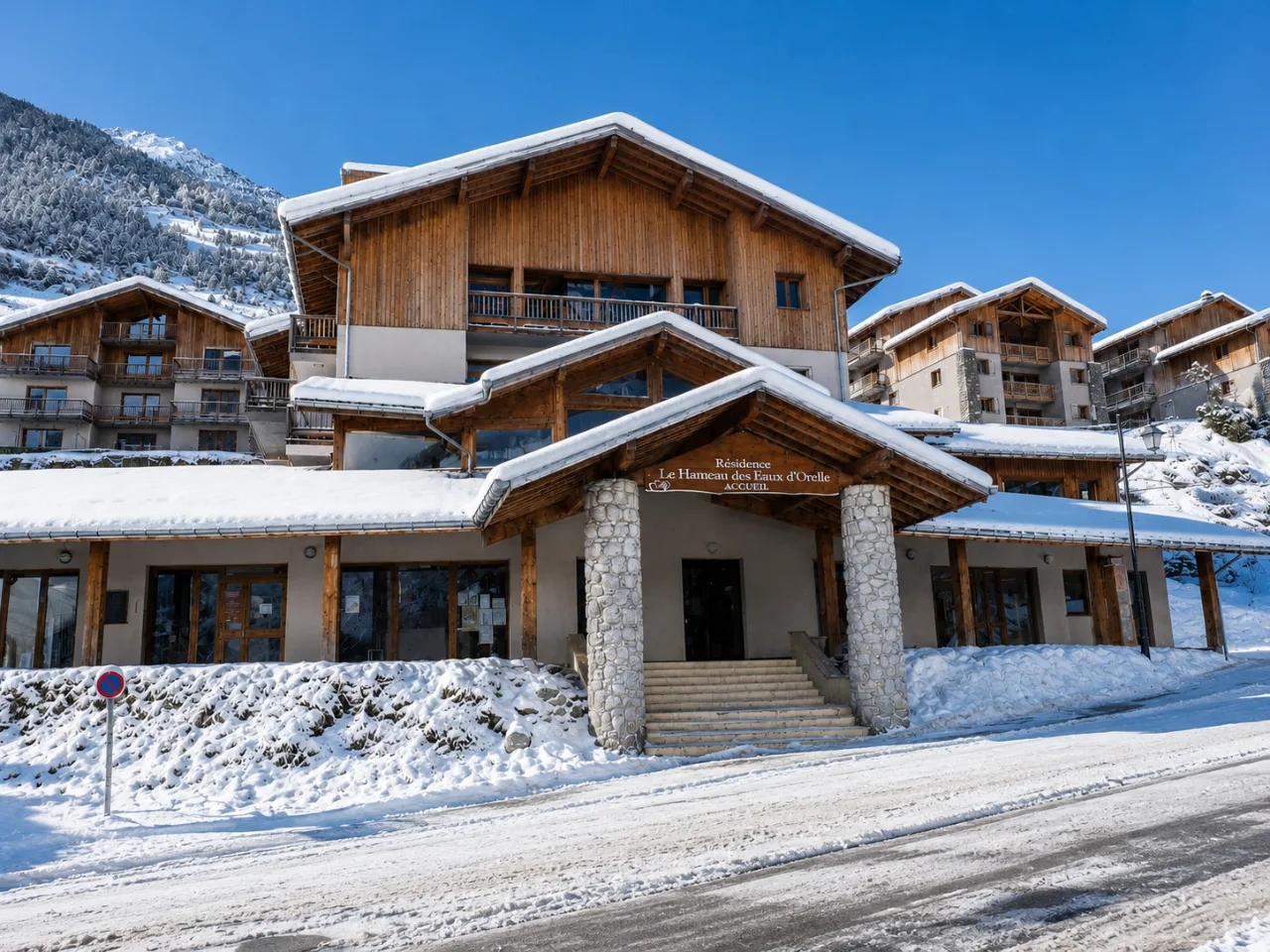 Zimowy widok na Résidence Le Hameau des Eaux d'Orelle w Orelle, Francja. Alpejskie apartamenty z drewnianymi fasadami pokryte śniegiem.