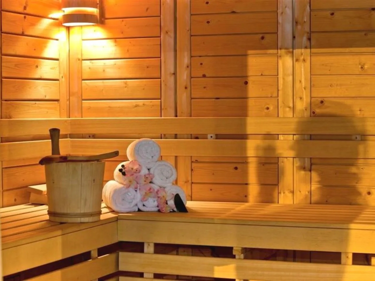 Drewniana sauna w L'Hameau, Orelle, Francja, z wiadrem, chochlą, zwiniętymi ręcznikami i różowymi kwiatami na ławce.