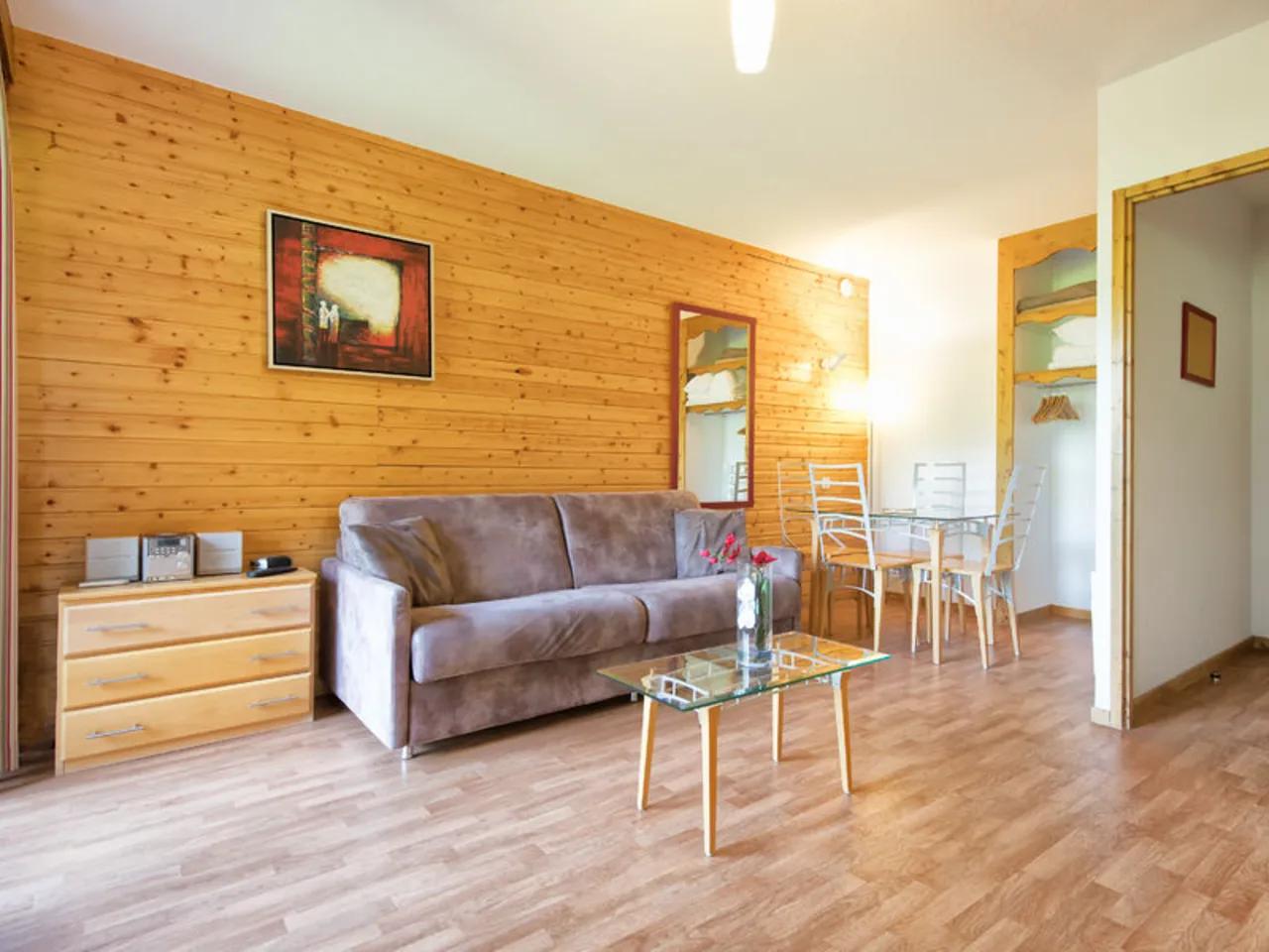 Przytulny salon z drewnianymi panelami, szarą sofą, szklanym stołem jadalnianym i komodą w apartamencie.