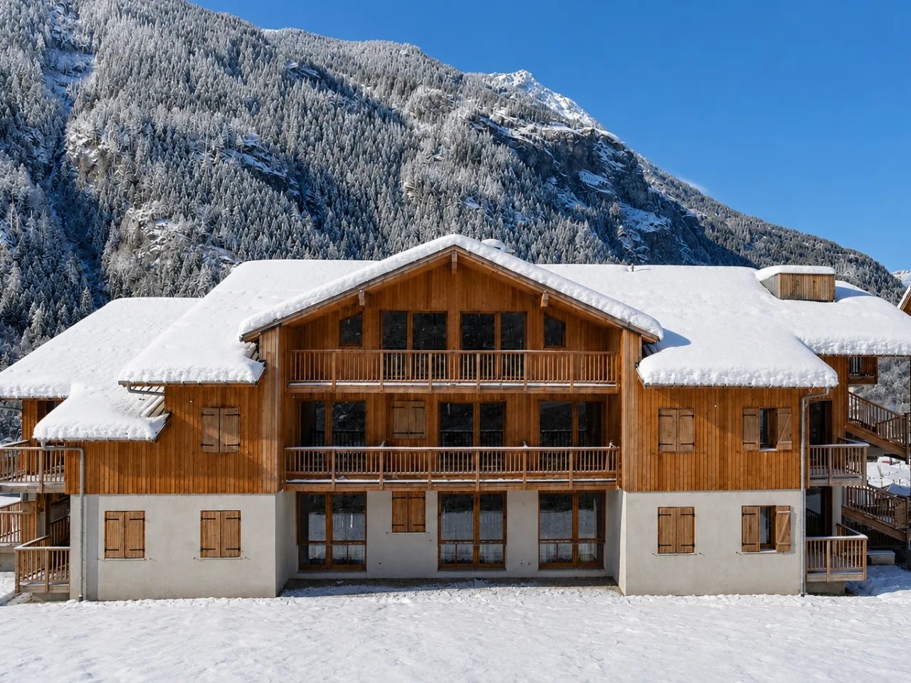 Zimowy widok na Résidence Le Hameau des Eaux d'Orelle w Orelle, Francja. Alpejskie apartamenty z drewnianymi fasadami pokryte śniegiem.
