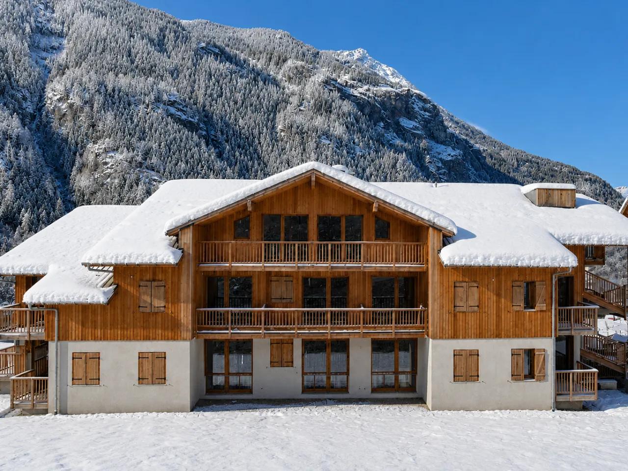 Zimowy widok na Résidence Le Hameau des Eaux d'Orelle w Orelle, Francja. Alpejskie apartamenty z drewnianymi fasadami pokryte śniegiem.