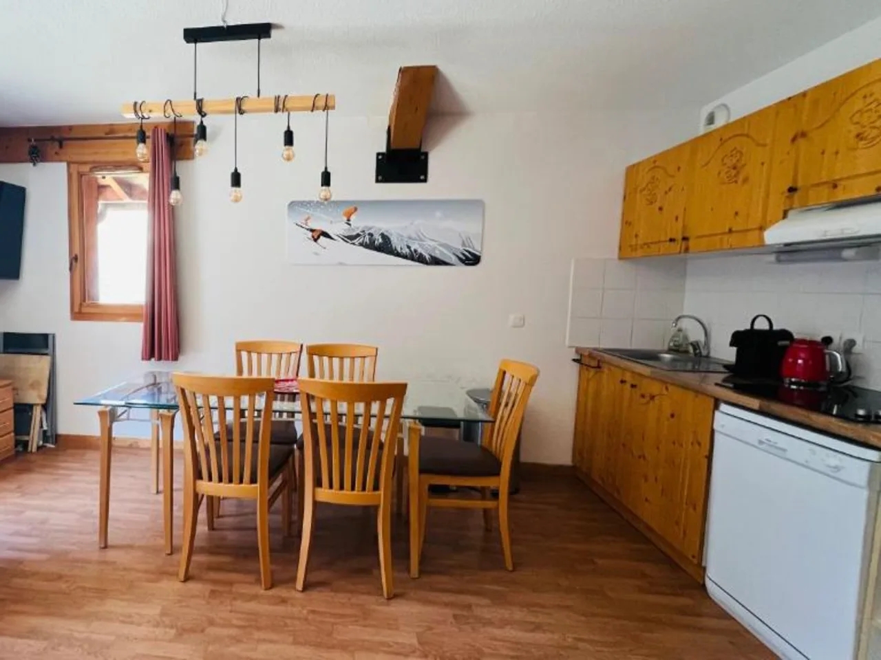 Wnętrze apartamentu L'Hameau w Orelle, Francja: salon z TV, aneks kuchenny i jadalnia z drewnianymi meblami.