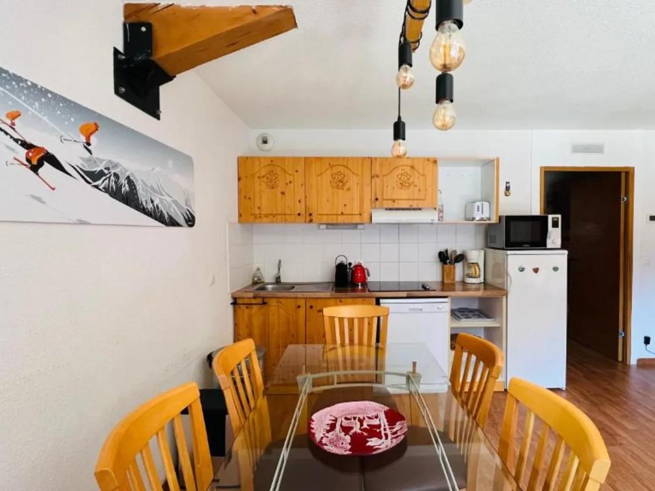 Wnętrze apartamentu w L'Hameau, Orelle, Francja: przestronna jadalnia ze szklanym stołem i drewniany aneks kuchenny.