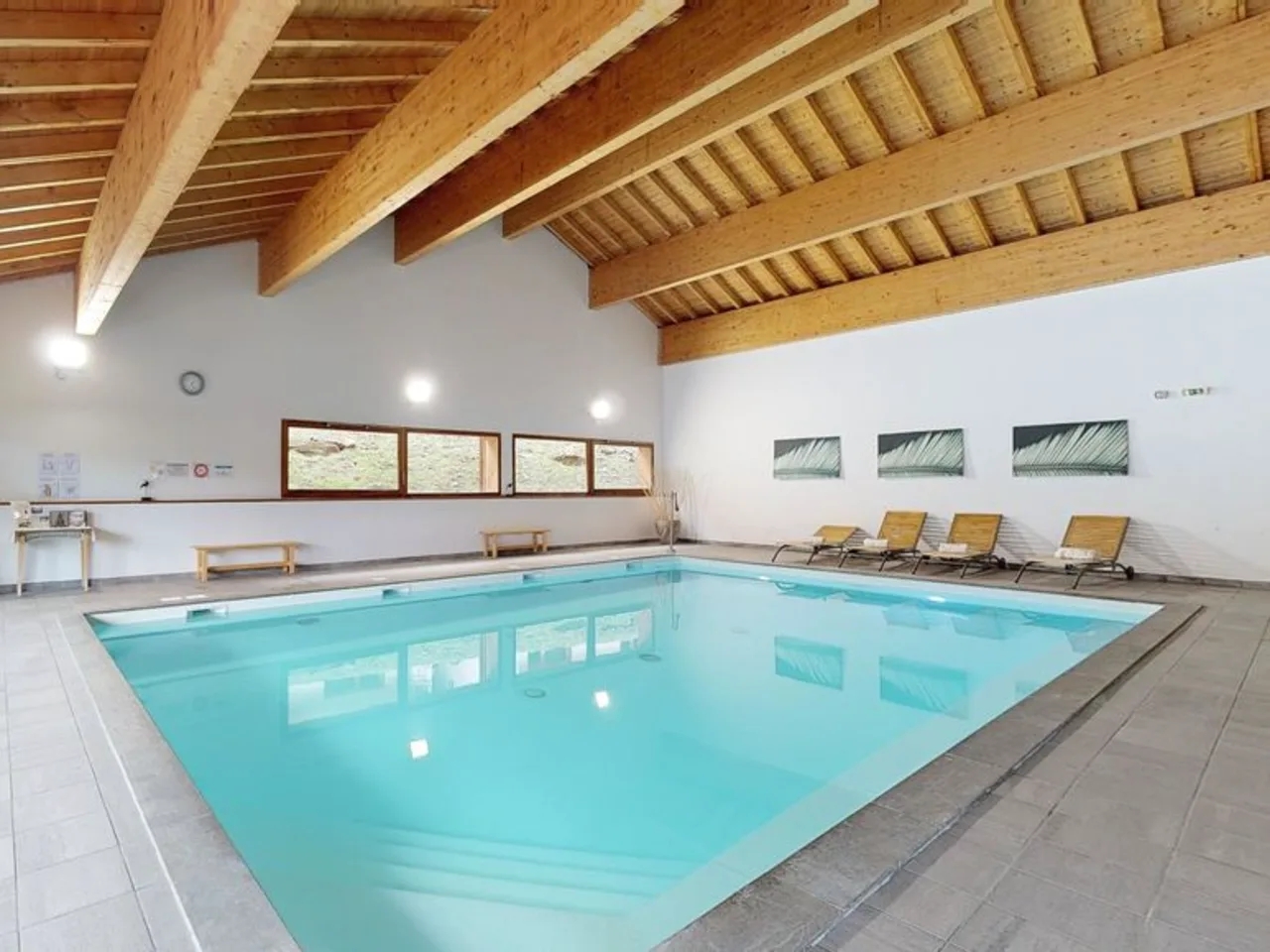 Kryty basen z lazurową wodą, drewnianym sufitem i leżakami, idealny do relaksu w hotelu lub apartamencie.