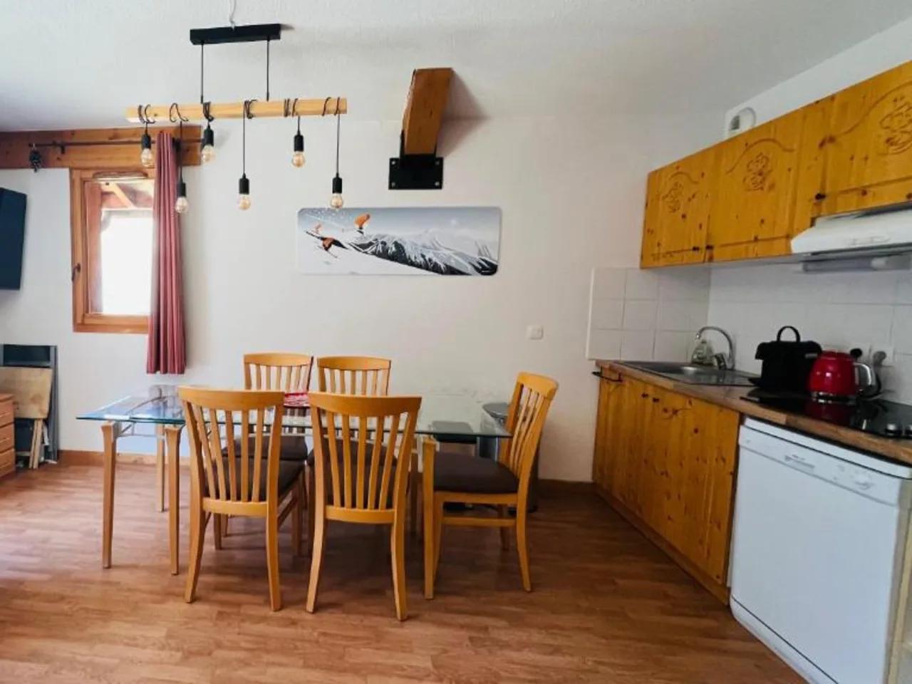 Wnętrze apartamentu L'Hameau w Orelle, Francja: salon z TV, aneks kuchenny i jadalnia z drewnianymi meblami.