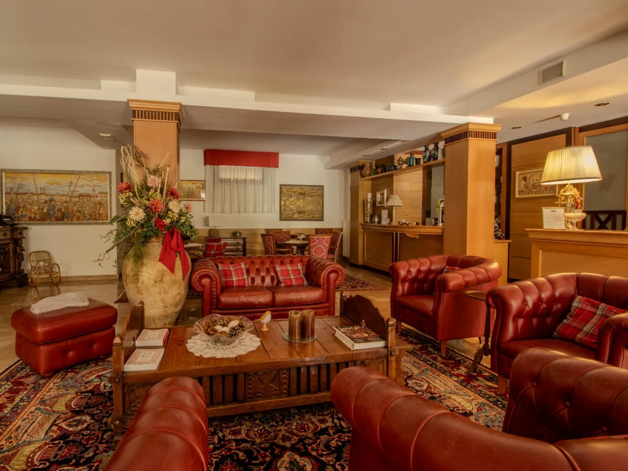 Elegancki i klasyczny salon hotelowy z czerwonymi sofami Chesterfield, ozdobnym perskim dywanem i dużymi bukietami kwiatów.