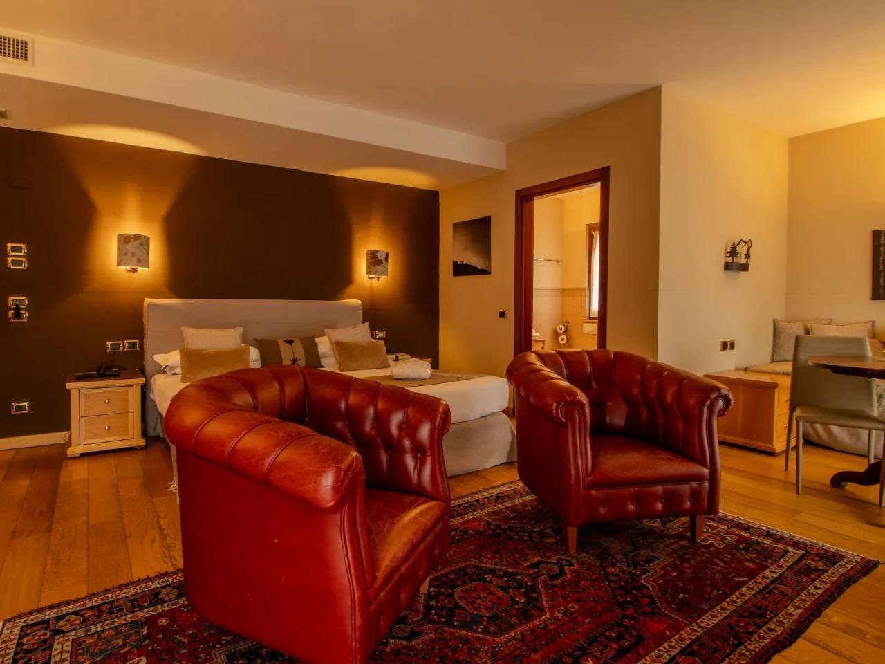 Luksusowy pokój hotelowy: czerwone skórzane fotele, duże łóżko, drewniana podłoga i orientalny dywan. Stylowe wnętrze.