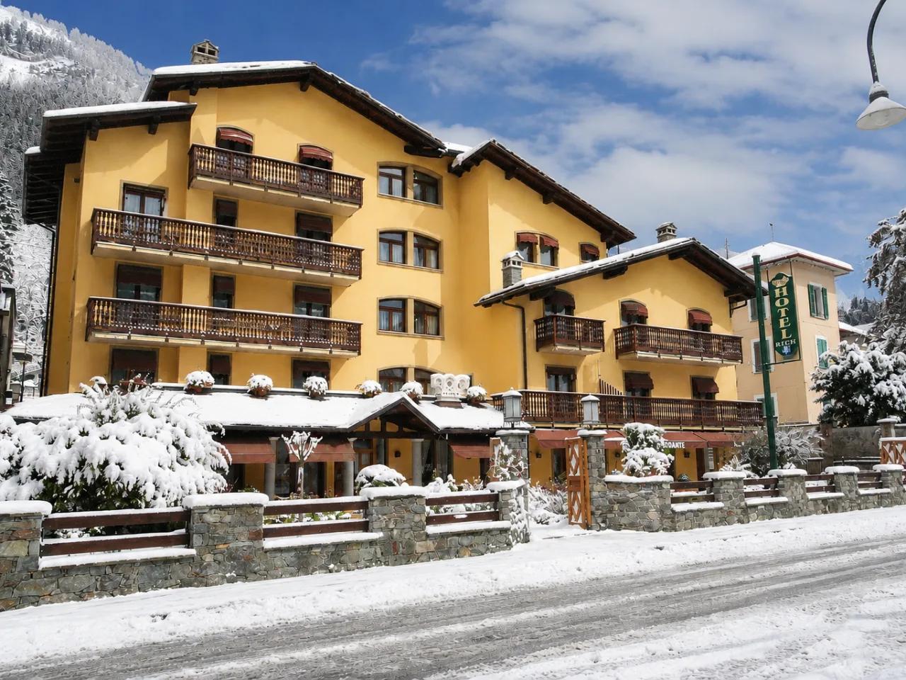 Hotel Paradise we włoskiej Aosta Saint Vincent zimą. Żółty budynek z balkonami, pokryty śniegiem, na tle gór.