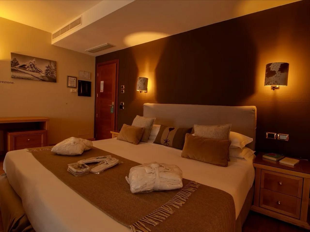 Przytulny pokój hotelowy z dużym łóżkiem, miękką pościelą, ciepłym oświetleniem i eleganckim wystrojem, idealny do relaksu.