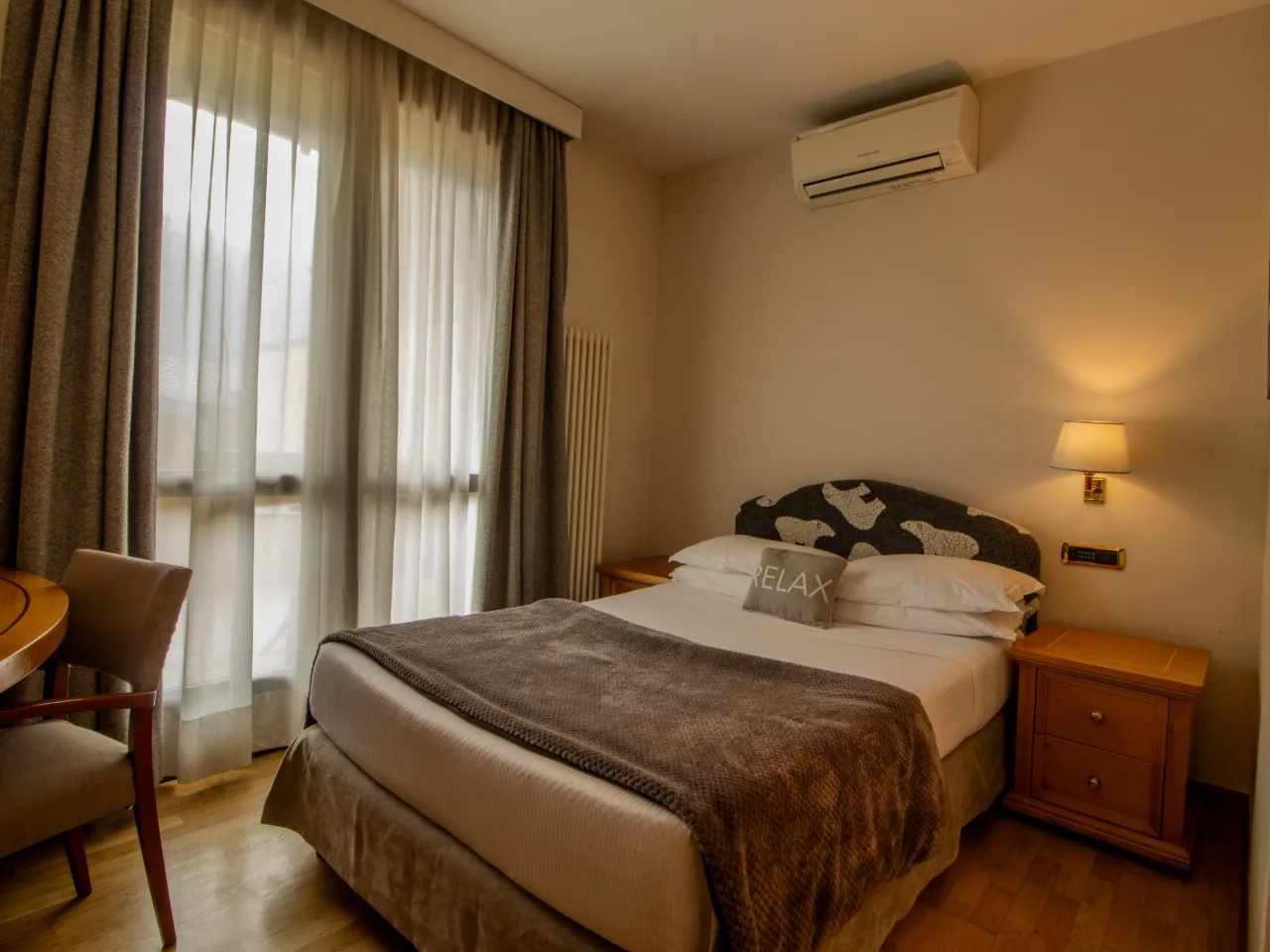 Przytulna sypialnia hotelowa z dużym łóżkiem, klimatyzacją i oknem z zasłonami, idealna do relaksu.