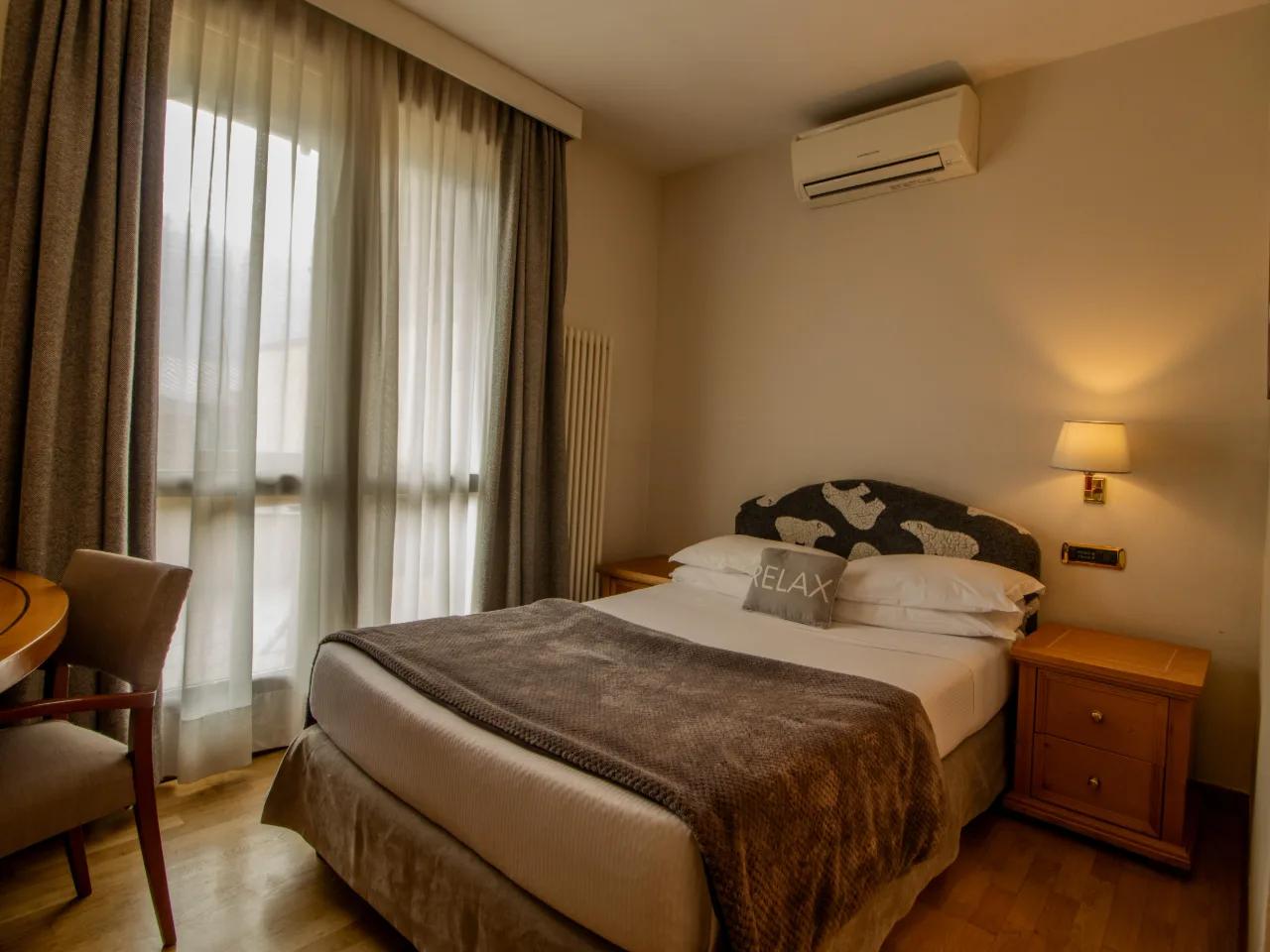 Przytulna sypialnia hotelowa z dużym łóżkiem, klimatyzacją i oknem z zasłonami, idealna do relaksu.