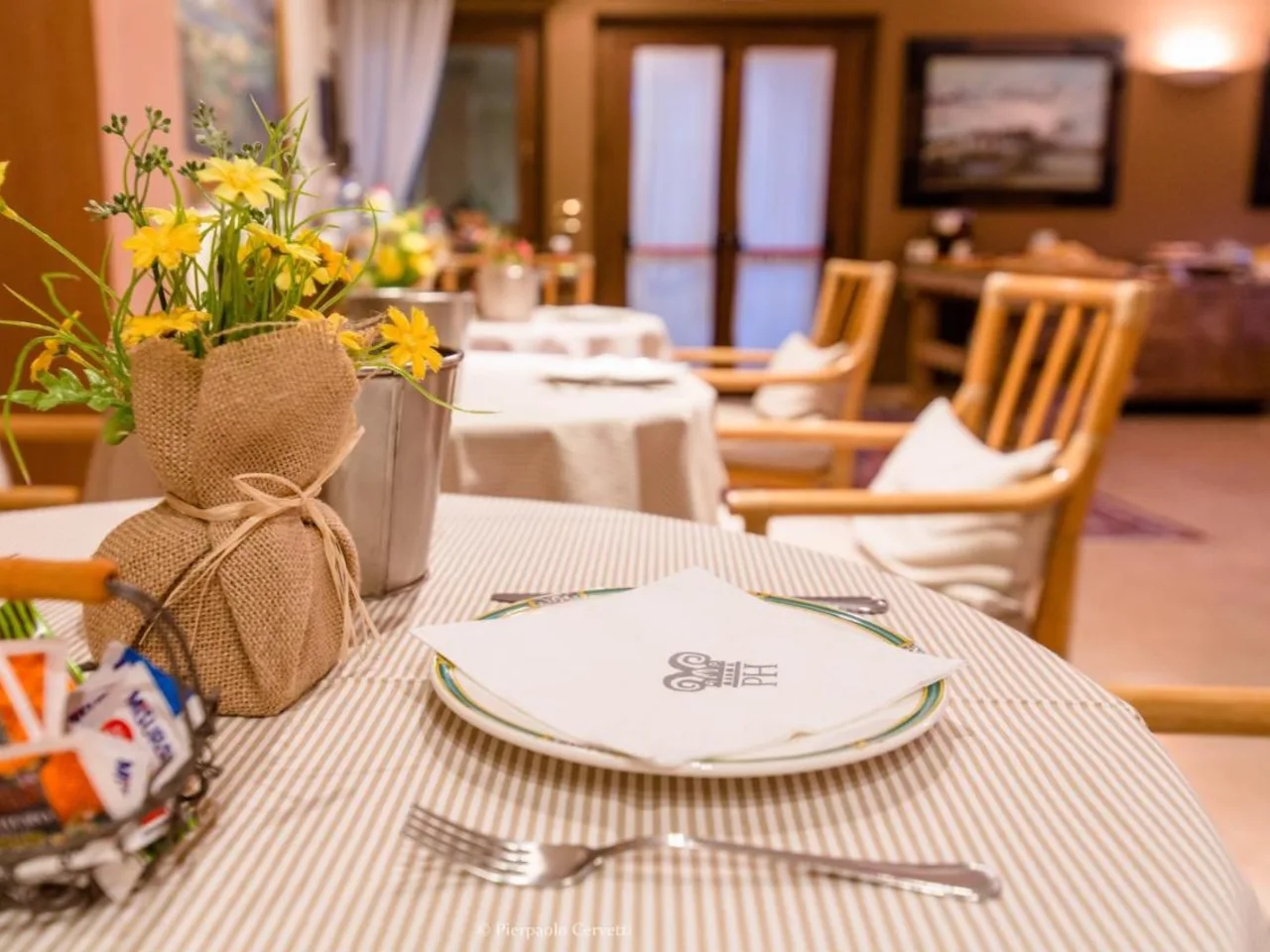 Nakryty stolik w restauracji z żółtymi kwiatami w jutowym wazonie, obrusem w paski i koszykiem cukru, idealny na śniadanie.