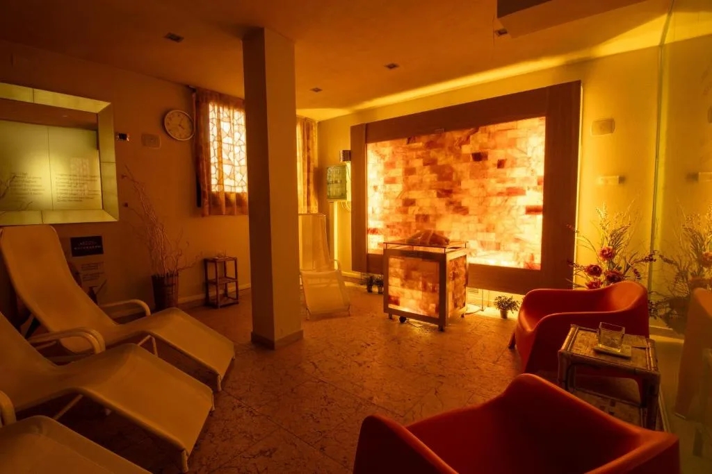 Przytulna strefa relaksu z podświetlaną ścianą solną, leżakami i czerwonymi fotelami w spa Paradise Saint Vincent we Włoszech.