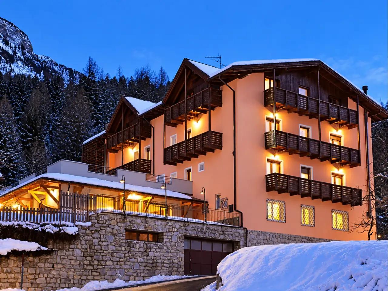 Zimowy widok na Park Bellevue w Val di Sole, Włochy. Oświetlony hotel z balkonami na tle ośnieżonych Alp.