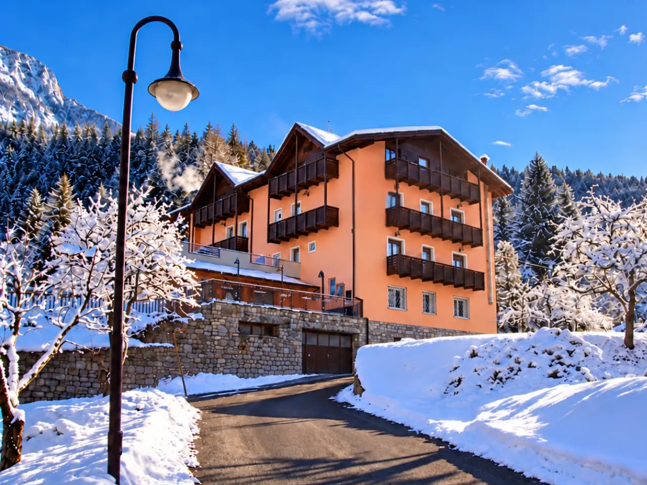 Park Hotel Bellevue w Val di Sole, Włochy. Zimowy, słoneczny dzień, hotel otoczony śniegiem i ośnieżonymi drzewami, w tle góry.