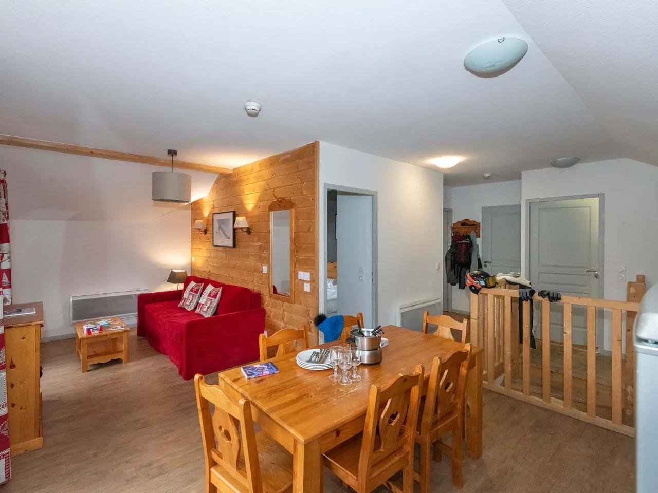 Przytulny salon z jadalnią w apartamencie górskim, czerwona sofa, drewniany stół, dekoracje w alpejskim stylu, idealny na wakacje.