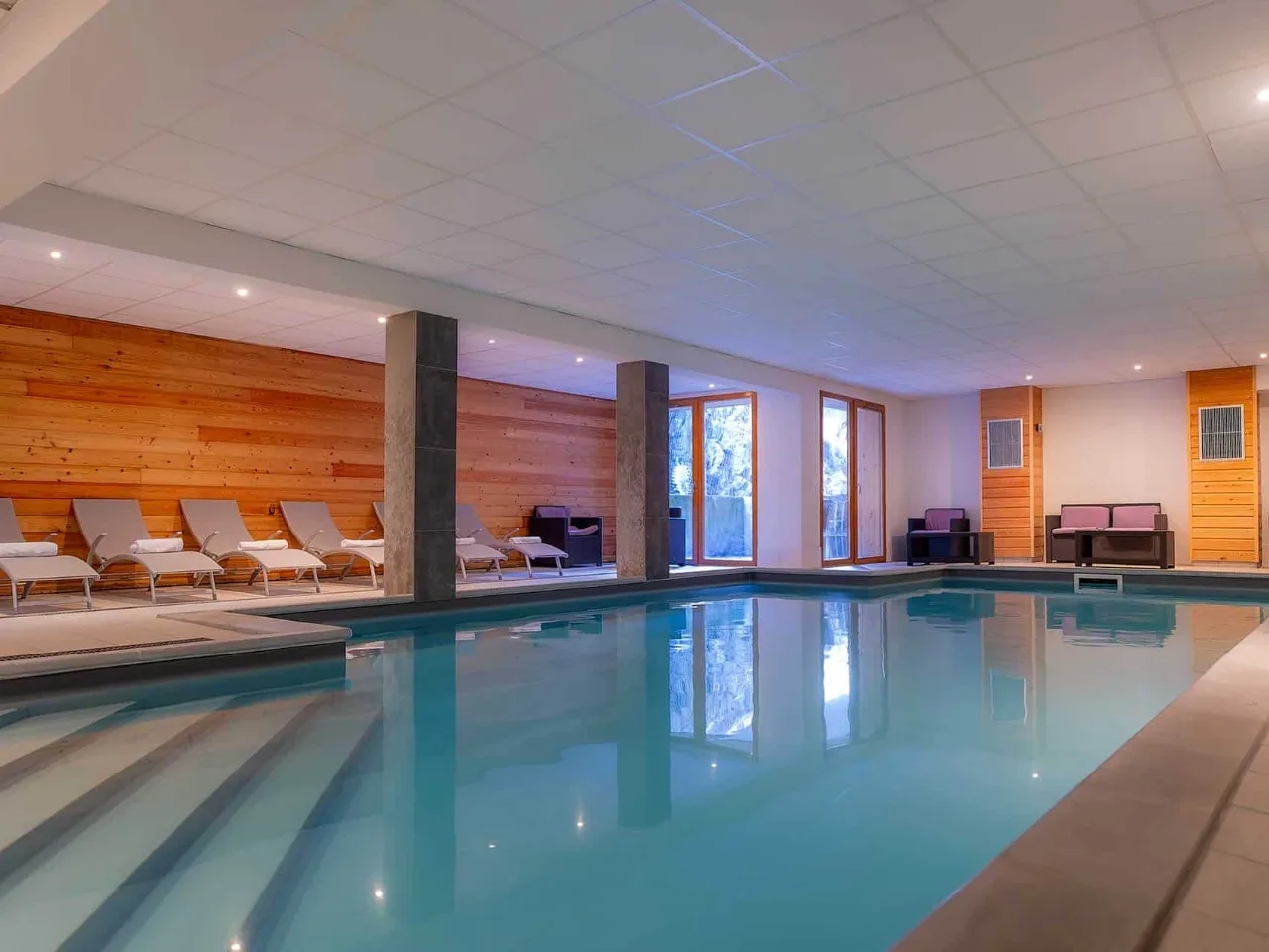 Nowoczesny basen hotelowy z błękitną wodą, leżakami i drewnianymi ścianami. Idealne miejsce na relaks i spa.