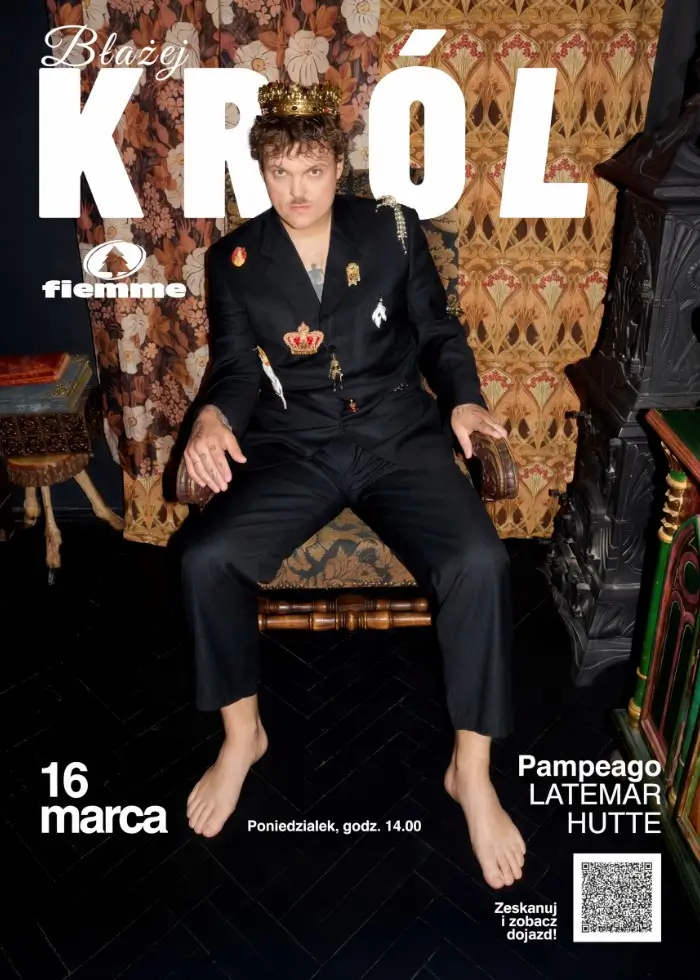 Plakat Błażeja Króla i fiemme. Artysta w koronie i czarnym garniturze, siedzący boso na krześle, na tle wzorzystej tapety. Promocja wydarzenia 16 marca.